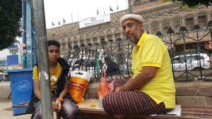 نياز عبد الزمد عيسى جالسًا على رصيف في ميدان التحرير يتناول الغداء مع ابنه لؤي البالغ من العمر 14 عامًا